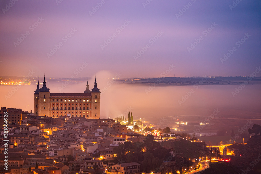 Sunrise in the historic and amazing Downtown Toledo. Alcazar is surrounded by fog. Foggy morning with city lights in Toledo, Spain.