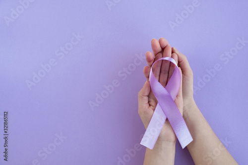 Womans hands hold purple epilepsy awarenes ribbon on light background. World epilepsy day, cancer day. Medicine and healthcare concept. Top view, copy space photo