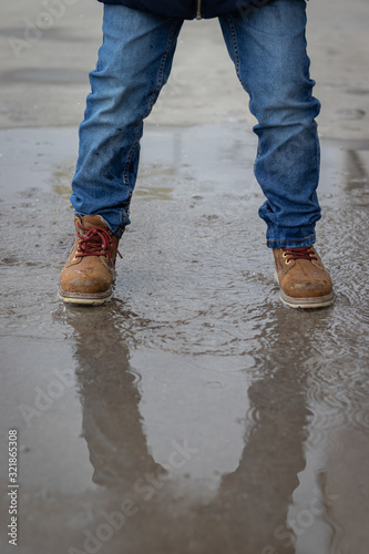 Water and fund with booths. Kid is jumping and splashing on a water mud in the street, wearinf jeans and brown boths photo