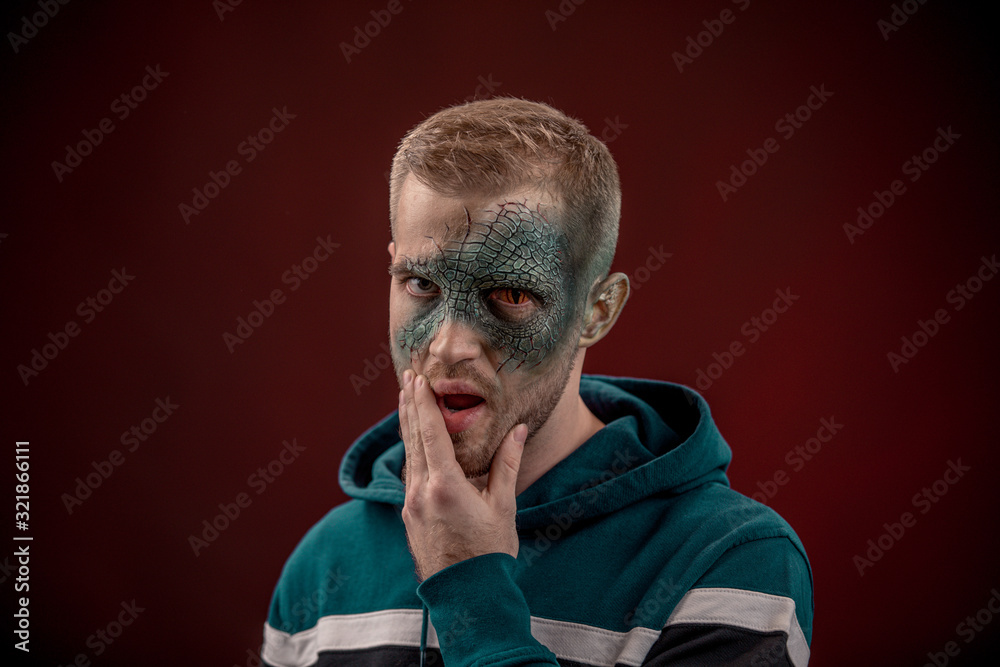 man with professional horror movie make-up green lizard on dark red background. lizard eye