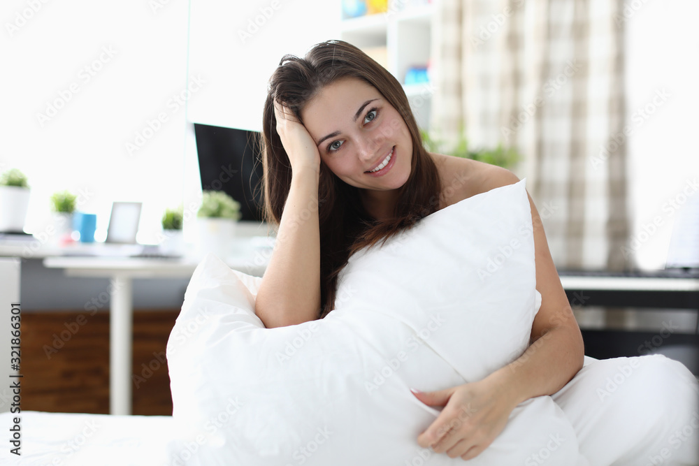 Happy girl wakes up in morning and sits on bed. Young woman is sitting under house under covers, pillow is lying on her lap. Style Girl room interior, bed and workplace with computer. Happy girl wakes up in morning and sits on bed. Young woman is sitting under house under covers, pillow is lying on her lap. Style Girl room interior, bed and workplace with computer.