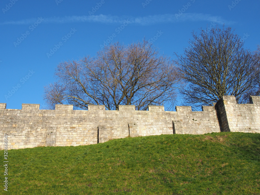 a view of the ancient medieval city walls of york with grass covered embankment and blue sky a view of the ancient medieval city walls of york with grass covered embankment and blue sky