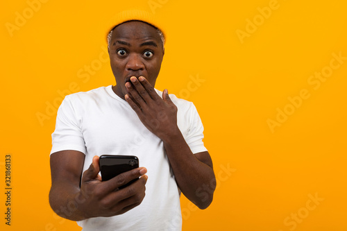 black american man looks in surprise on the phone on a yellow background