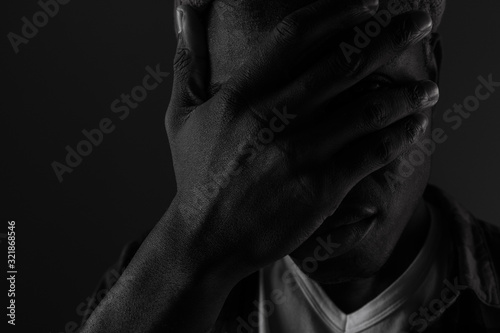 Close-up portrait of a dark-skinned guy with eyes closed by hand in black and white light