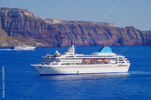 White classic Celestyal Cruises cruiseship or cruise ship liner anchored in bay of volcanic Greek Island of Santorini with cliffs and city of Oia in background in summer on blue sea and sky photo