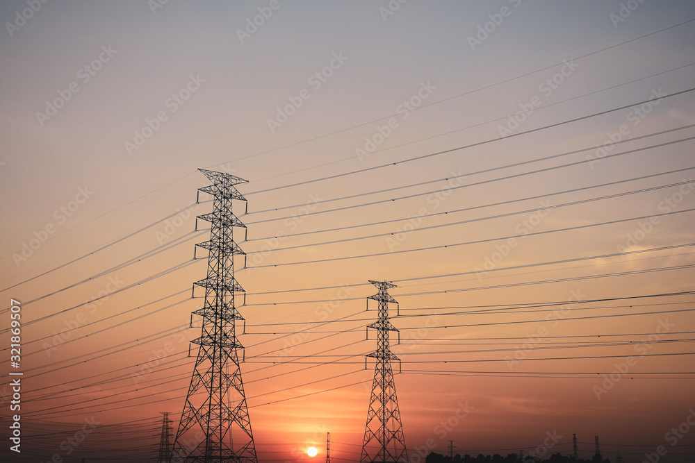 Silhouette High voltage electric tower line in cornfield at sunset.