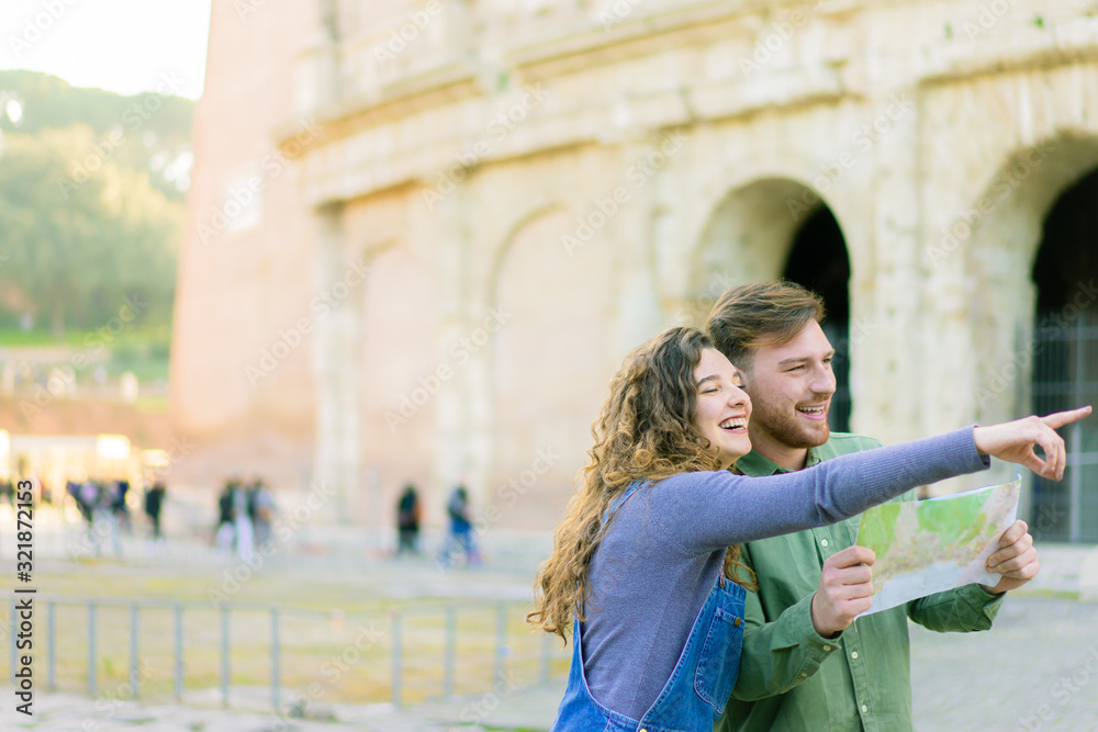 Fototapeta premium Young traveler couple using local map, girl pointing forward . Happy tourists visiting famous landmarks. Honeymoon trip, tourist, love holiday and vacation travel concept - Image