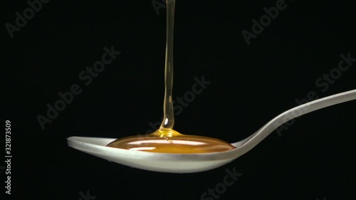 Slow motion shot : Close up honey dripping on the stainless tea spoon on black back ground.