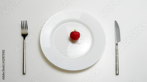 The concept of diet and healthy lifestyle. Top view of a plate in which lies a radish, with a fork and a knife, is on the table.