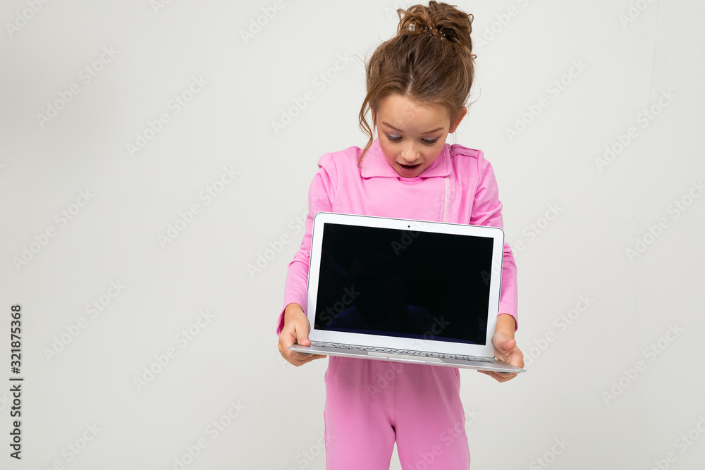 Closeup portrait of attractive funny charming baby in pink costume showing laptop screen with mock up on white background