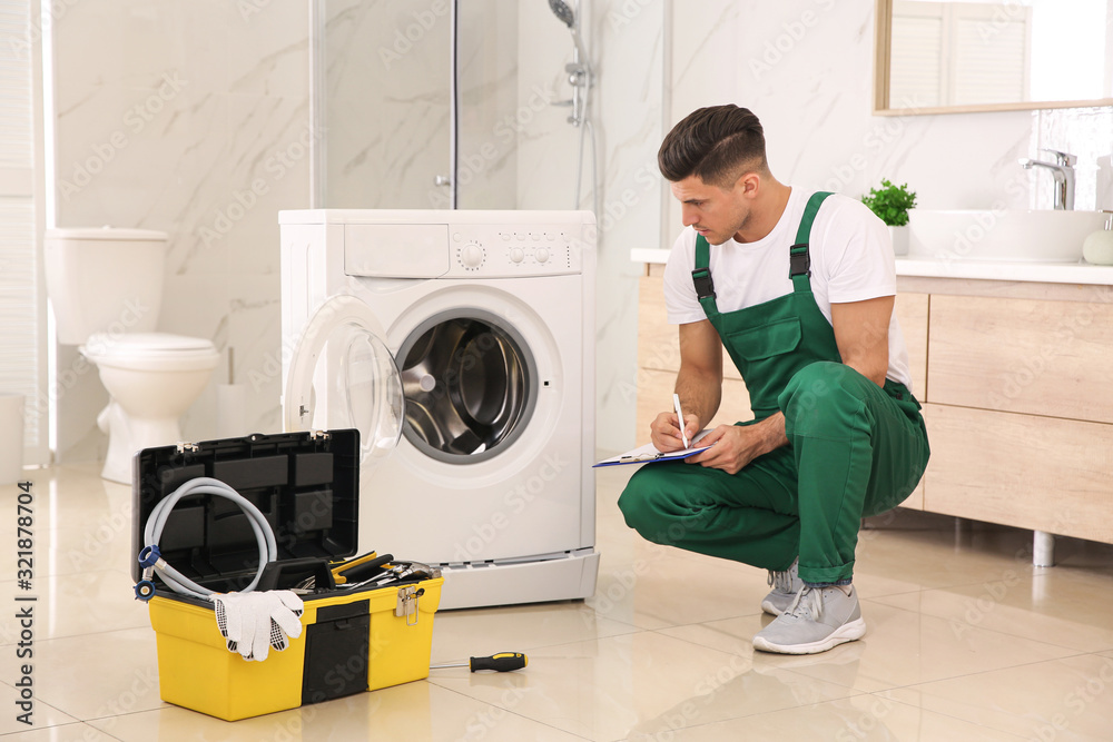 Professional plumber repairing washing machine in bathroom