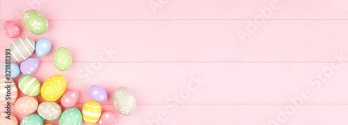 Easter banner with pastel colored egg corner border over a pink wood background. Top view with copy space.