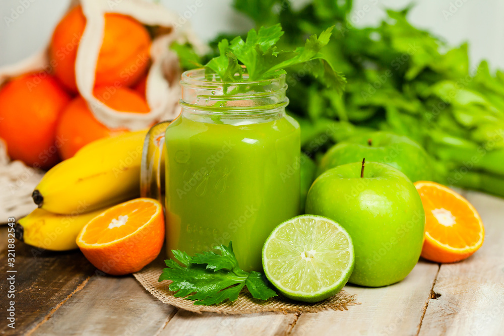 Healthy food and vegan diet concept - mason jar of fresh green juice or smoothie with celery, orange, banana, apple. Antioxidant detox beverage with raw ingredients. Wooden background. Healthy food and vegan diet concept - mason jar of fresh green juice or smoothie with celery, orange, banana, apple. Antioxidant detox beverage with raw ingredients. Wooden background.