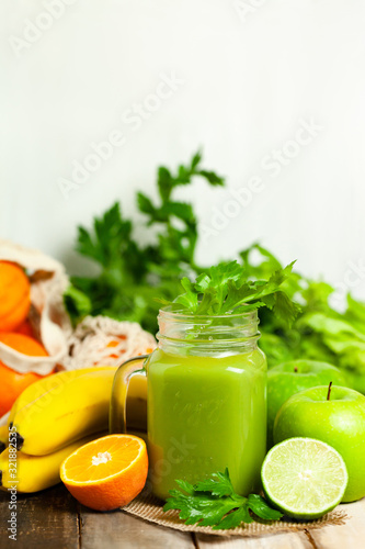 Healthy food and vegan diet concept - mason jar of fresh green juice or smoothie with celery, orange, banana, apple. Antioxidant detox beverage with raw ingredients. Wooden background, copy space