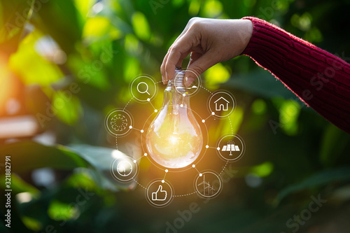 hand holding light bulb against nature, icons energy sources for renewable. photo