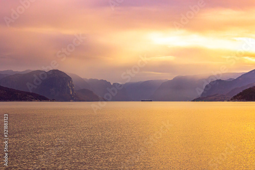 Mesmerizing scene in the Lysefjord with sunlight breaking through the foggy and cloudy sky with a range of mountains, Norway