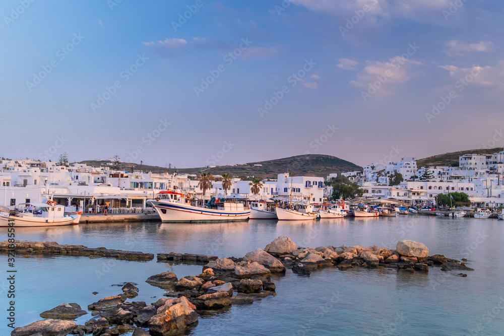 Panoramic view of sunset at popular tourist attraction in Paros island, Naousa town. Promenade zone with bars and restaurants along harbor. Aegean Sea and boats in quay. Amazing evening in Greece