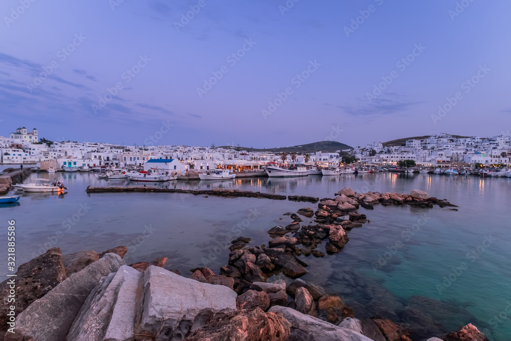 Panoramic view of sunset at popular tourist attraction in Paros island, Naousa town. Promenade zone with bars and restaurants along harbor. Aegean Sea and boats in quay. Amazing evening in Greece
