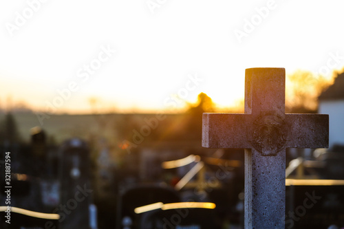 Canvas Print Cruz de un cementerio de piedra con el reflejo del sol por detrás al atardecer