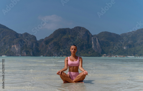 Beautiful girl in a pink swimsuit practices yoga in the ocean. photo