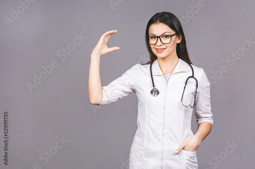 Portrait of cheerful young female doctor with stethoscope over neck looking at camera isolated on grey background. Presenting your product.