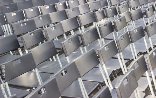 Lots of black chairs near a hedge in the open air. Chairs