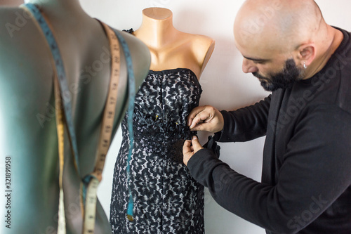 Fashion designer using needle to sew black fabric on top part of the dress.