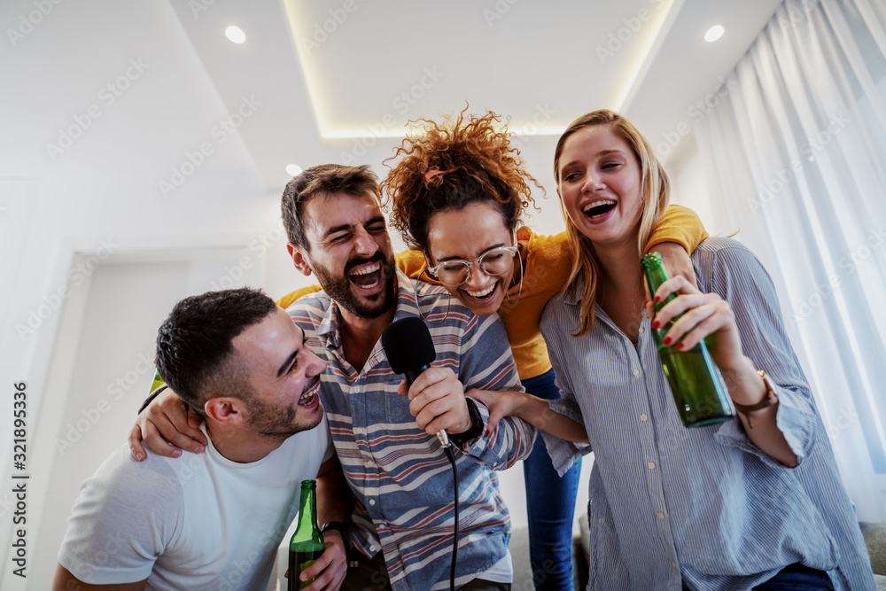 Group of friends having karaoke party at home. Man holding microphone while other ones holding beer.