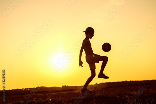 Fototapeta Naklejka Na Ścianę i Meble -  Boy playing with ball in nature in hot evening, silhouette of playing child at sunset in countryside