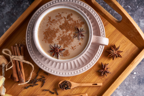 Masala tea in cup with spices ginger, cinnamon, anise, black pepper on gray sone background