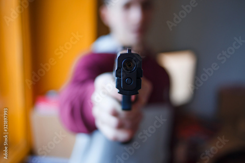 a young guy with a blurry face pointed a gun into the lens of a gun in his hand the barrel of a gun