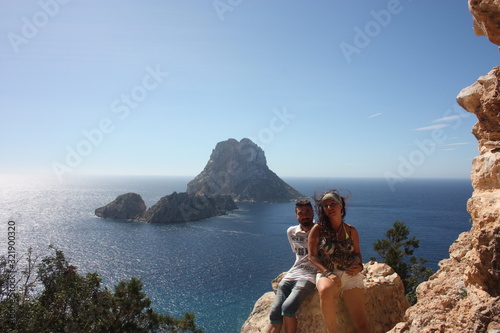 young caucasian couple in love on a rock of a steep cliff in the rocky desert of cala d'hort in front of the magical island of Es Vedra photo