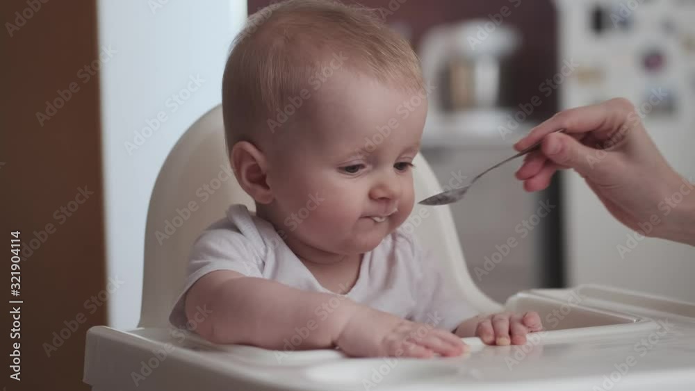 Cute little baby feeding with a spoon at the table, infant eating meal foods. 4k 50 fps Cute little baby feeding with a spoon at the table, infant eating meal foods. 4k 50 fps