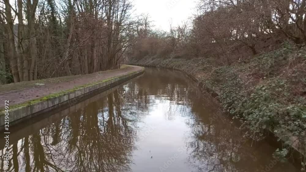 View from the bow of narrowboat traveling through English rural countryside scenery on British tree lined waterway canal View from the bow of narrowboat traveling through English rural countryside scenery on British tree lined waterway canal