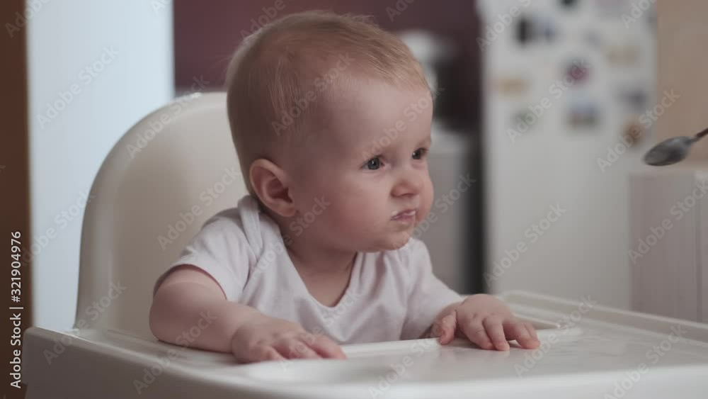 Cute little baby feeding with a spoon at the table, infant eating meal foods. 4k 50 fps
