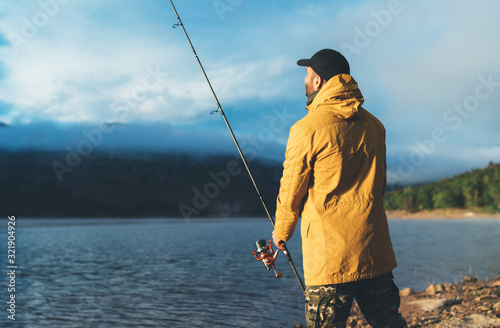 fishery concept, fisherman enjoy hobby sport with fishing rod on evening lake, catch fish on background blue sky, holiday relaxation vacation