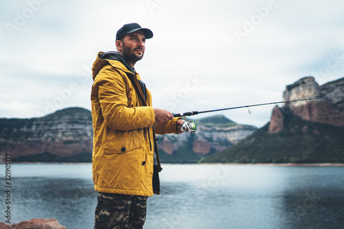 beard fisherman hold in hands fishing rod, man enjoy hobby sport on mountain river, person catch fish on background nature, relax fishery concept photo