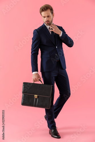 Powerful businessman holding a briefcase and fixing his collar photo