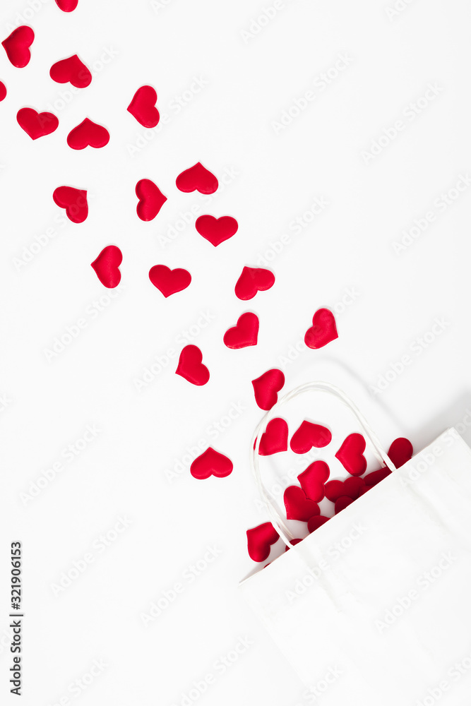 Elegant composition for Valentine's Day. Paper white gift bag, red hearts on white background. Valentine day, 8th march, Mother day background. Love concept. Flat lay, top view, copy space