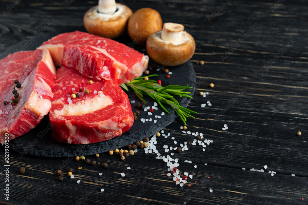 Three pieces of juicy raw beef on a stone cutting board on a black wooden table background. Three pieces of juicy raw beef on a stone cutting board on a black wooden table background.