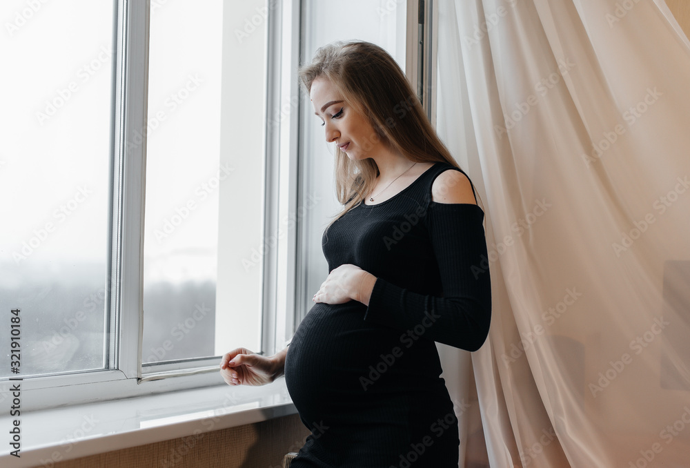 A pregnant girl is breathing fresh air from the window