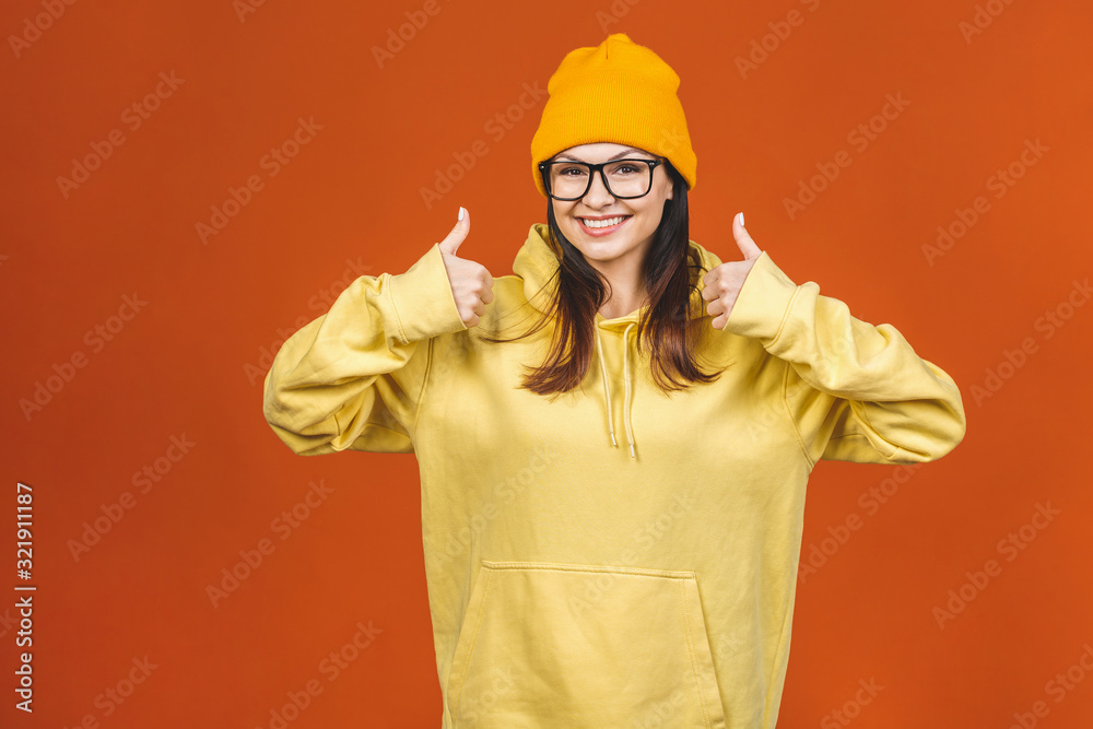 People, youth, leisure and lifestyle concept. Fashionable beautiful young Caucasian young female student wearing stylish clothing laughing, pointing finger. Isolated over orange. Thumbs up. People, youth, leisure and lifestyle concept. Fashionable beautiful young Caucasian young female student wearing stylish clothing laughing, pointing finger. Isolated over orange. Thumbs up.