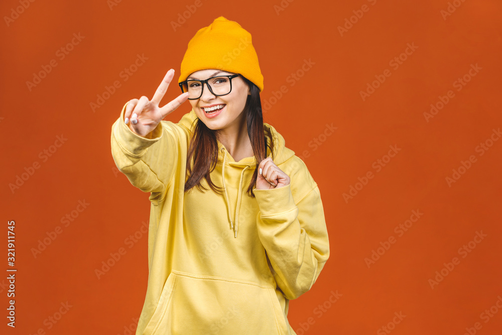 People, youth, leisure and lifestyle concept. Fashionable beautiful young Caucasian young female student wearing stylish clothing laughing, pointing finger. Isolated over orange.