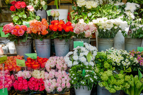 Front view of colourful various bouquet of roses and flowers in metal vases on shelf in front of flower stall or floral shop at farmer market in Europe. Typical atmosphere of flower store. 