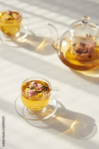 Cup of rose tea on abstract background of natural curtain shadow falling on white table, in rays of sunlight. Minimalism concept for design. Sunny summer day. Copy space.