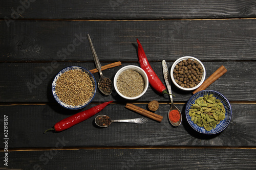 mix of spices baharat in bowls and vintage spoons on black wooden  background with copy space