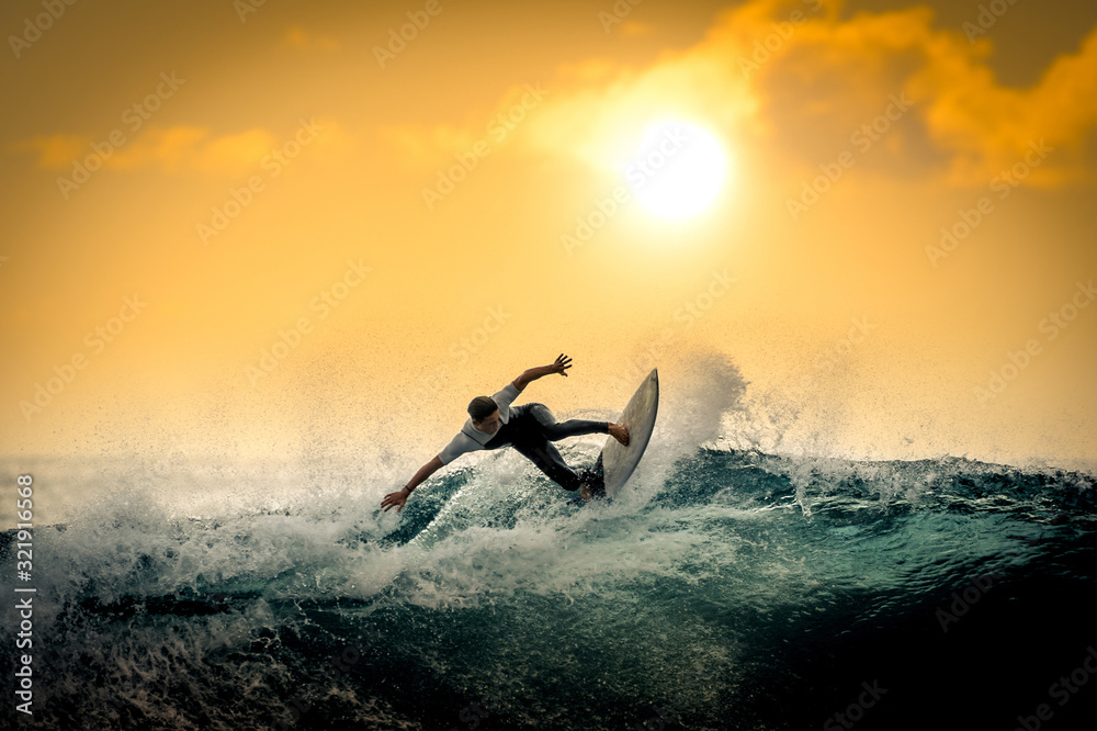 Young surfer with with wetsuit enjoying big waves in Tenerife, Canary Islands. Sporty boy riding his surf board on the ocean wave. Brave teenager making tricks on the rough sea during a competition.