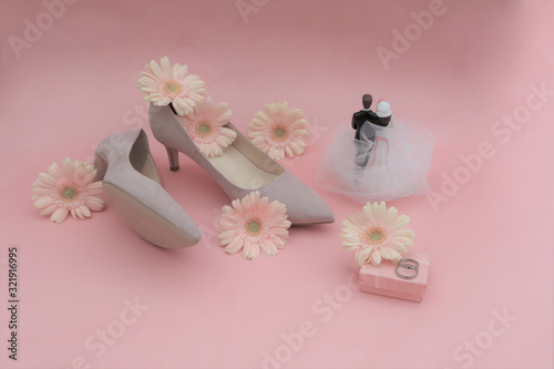 wedding concept. gerbera flowers, rings, beige shoes, newlywed figurine on a pink background.