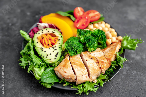 Bowl Buddha. chicken, broccoli, chickpeas, pumpkin, avocado, carrot, tomato, lettuce on a plate on a stone background