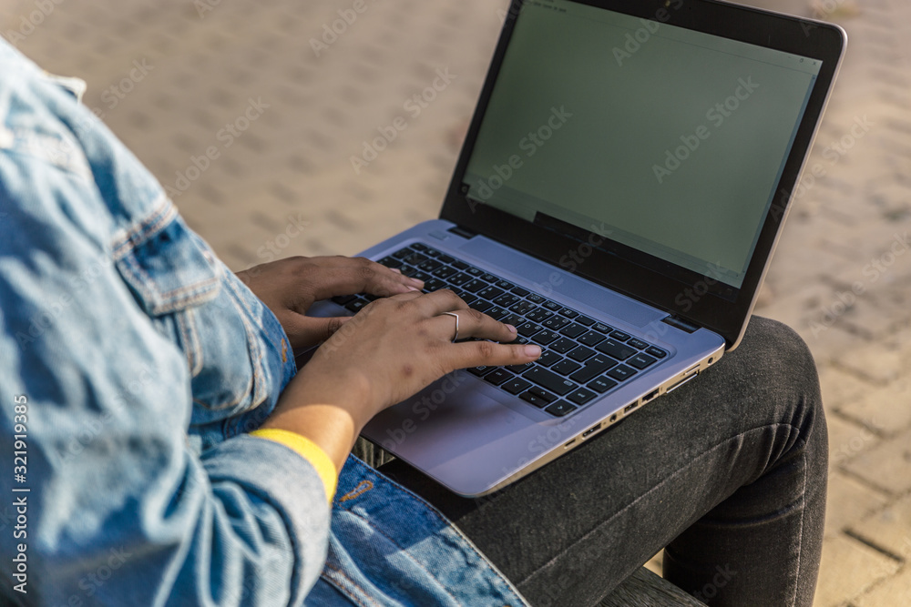 Fototapeta premium View of the hands of a woman typing on her laptop sitting on a park bench
